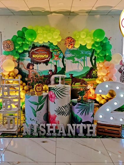 A classic Jungle Book theme for a second birthday. The stage is set with a lush green balloon arch, character cutouts of Mowgli, Baloo, and friends, and large marquee letters and numbers for a personalized touch.