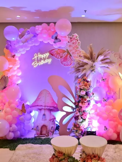 A magical butterfly-themed birthday party setup. This enchanted forest scene features pastel balloon arches, whimsical mushroom props, and a glowing 'Happy Birthday' sign, perfect for a child's fantasy party.