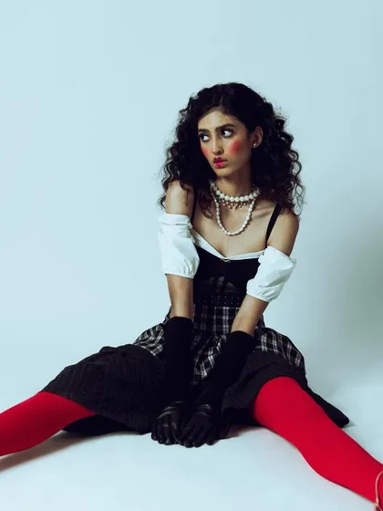 A full body shot of the dramatic doll makeup concept. The styling with red tights and black gloves adds to the theatrical and editorial feel of the photoshoot.