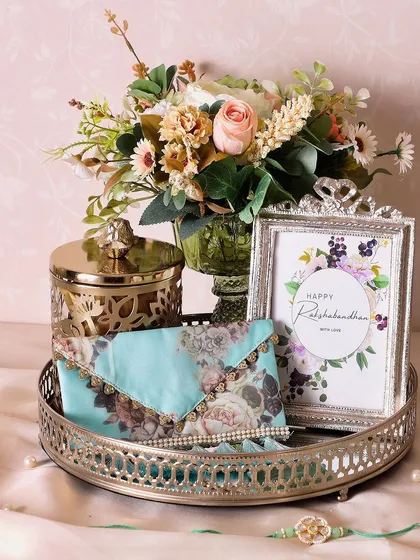 The Silver Oasis Rakhi Hamper combines tradition with elegance. It features a silver tray, photo frame, flower stand, and a metal jar of our cookies.