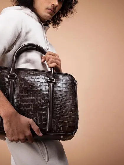 A minimalist campaign shot for Eské Global, focusing on a men's crocodile-texture briefcase. The neutral background and simple styling ensure the focus remains on the craftsmanship and design of the bag.