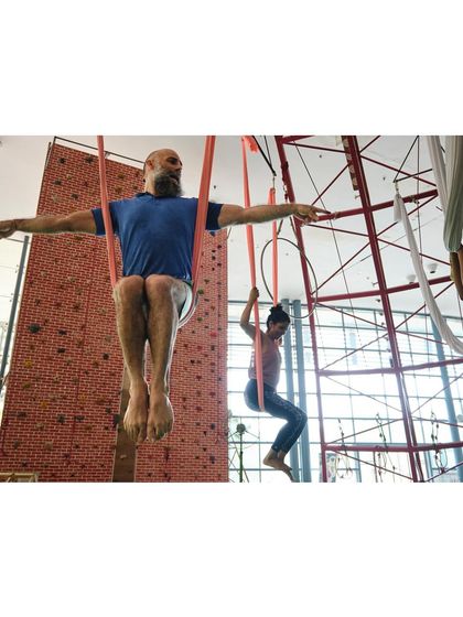 A group of students practice a seated pose in their hammocks, creating a sense of shared energy and focus in the class.