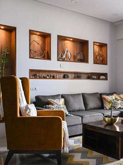 This living room is a perfect example of blending different styles. It combines a contemporary grey sofa and a modern partition with a classic mustard wingback chair and wooden display niches for a layered, eclectic look.