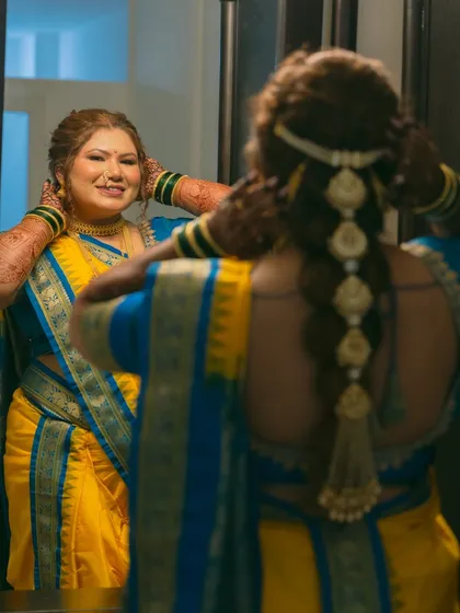 A moment of reflection. The bride admires her look in the mirror, showing off her traditional braided hairstyle adorned with flowers and her radiant makeup.