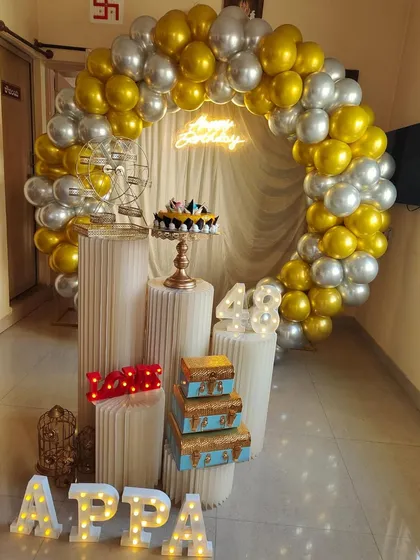 For this 48th birthday, I created a classy gold and silver balloon arch to frame the celebration space. The setup features custom marquee letters spelling "APPA", light-up numbers for the age, and a "Happy Birthday" neon sign, all brought together with decorative pedestals and props.