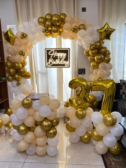 An elegant 37th birthday setup with a circular balloon arch in cream, white, and gold. The decor is completed with a neon sign and gold foil number balloons.