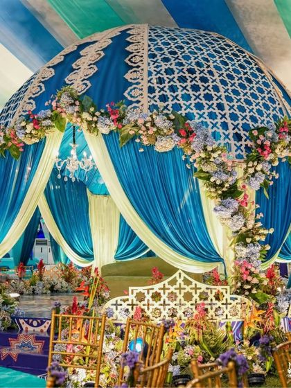 A close-up of the magnificent dome-shaped mandap. The intricate white lattice work on the blue dome, combined with floral decorations, makes it a stunning centerpiece for the ceremony.