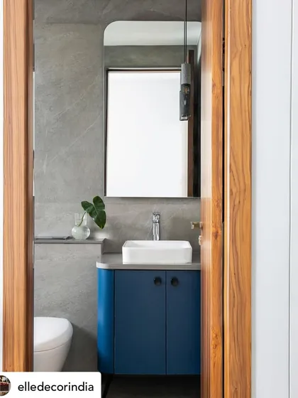 This bathroom features a bold blue vanity that adds a pop of color to the grey stone tiles. The design is clean, modern, and functional, with a vessel sink and a simple mirror.