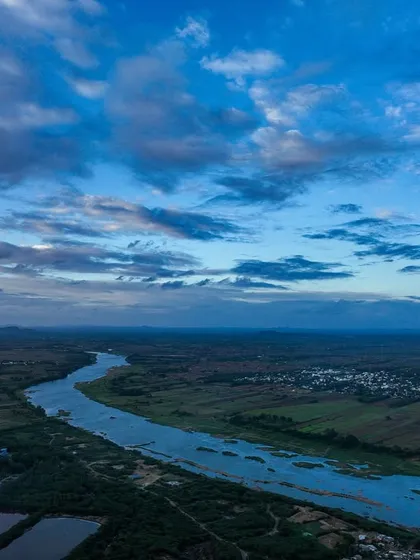 A river flows through the Karnataka landscape under a beautiful blue sky.