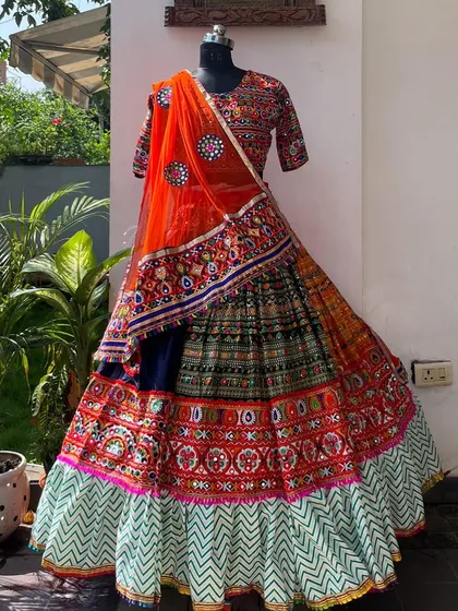 A stunning lehenga with a zig-zag patterned border and a bright orange mirror-work dupatta. The colors are perfect for the festive season.
