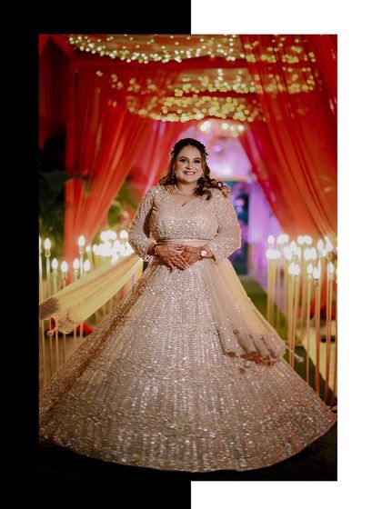 The bride, Pooja, looking radiant in her shimmering lehenga against a backdrop of red drapes and fairy lights.