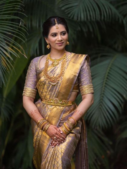 A stunning portrait amidst lush greenery. Her classic bridal makeup looks fresh and timeless, a perfect complement to the traditional setting.
