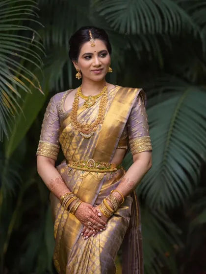 A stunning portrait amidst lush greenery. Her classic bridal makeup looks fresh and timeless, a perfect complement to the traditional setting.