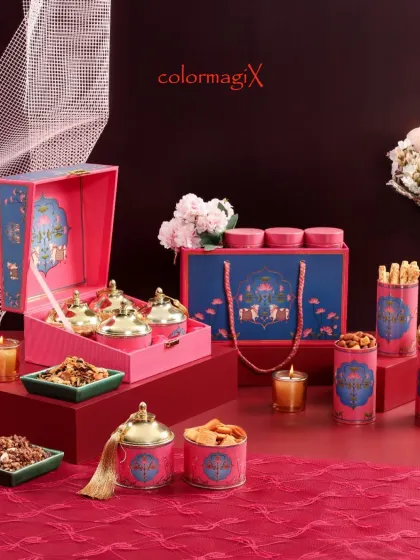 This vibrant pink and blue Diwali hamper is a feast for the eyes. It features ornate jars with golden lids for dry fruits and snacks, perfectly complemented by lit candles to enhance the festive ambiance.