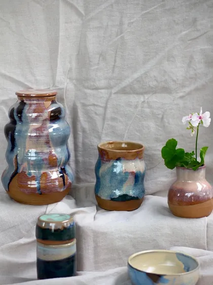 The same collection of wavy vases and bowls, with a small bud vase holding a delicate flower.