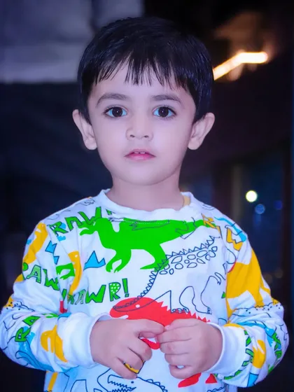 A close-up portrait of a young boy in a colorful dinosaur-themed shirt. His direct gaze and serious expression make for a compelling photo.