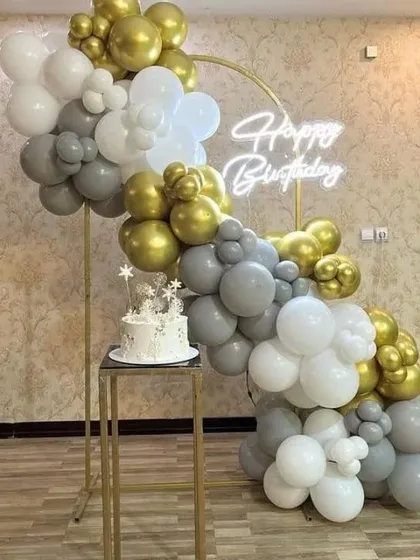 A minimalist and chic birthday setup with a gold, grey, and white balloon garland on a gold stand, perfect for a cake-cutting ceremony.