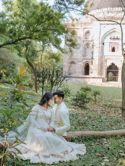 A romantic portrait of a couple sitting on a log in a historic park, surrounded by ancient ruins and greenery.