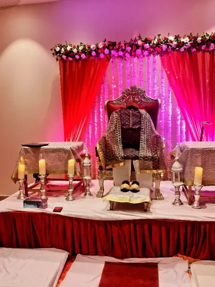 Another beautiful setup for a 'Jai Guruji' Satsang, featuring a regal seat, pink and red fabrics, and soft lighting to create a peaceful and devotional atmosphere.