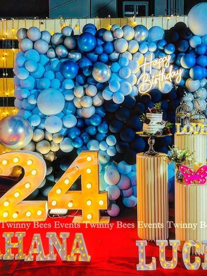 A cool blue-themed decoration for Sahana's 24th birthday. The setup includes a full balloon wall in shades of blue, a "Happy Birthday" neon sign, and marquee numbers and letters for a personalized touch.