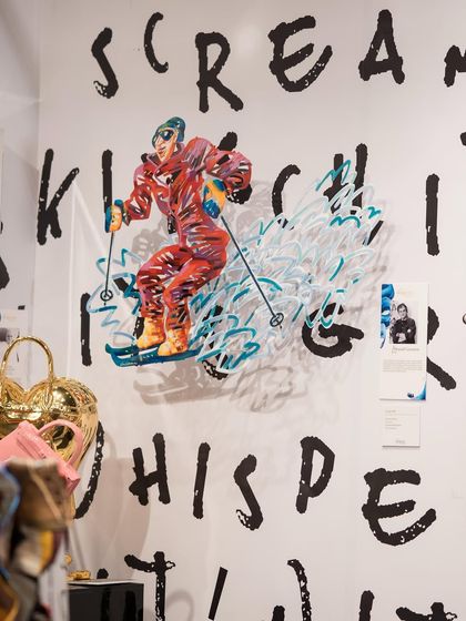 An action-packed wall sculpture of a skier, rendered in a vibrant, graphic style. This piece adds a sense of motion and energy to the gallery wall, set against a backdrop of bold, hand-painted text.