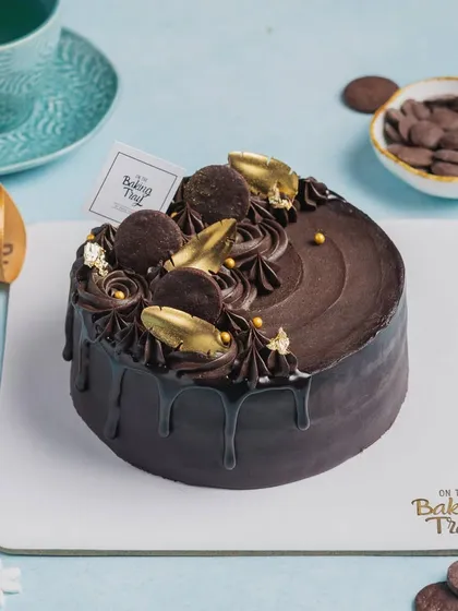 This is my signature OTBT Celebration Cake. It has a moist chocolate sponge, smooth ganache, and is decorated with swirls, mini cookies, and an edible gold feather for a touch of luxury.
