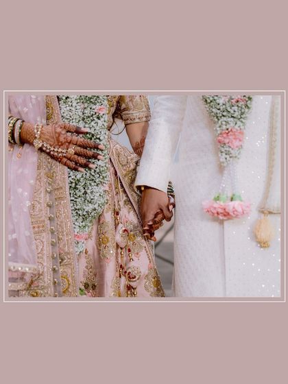 A close-up detail shot of the couple holding hands, showing the bride's intricate henna and the garlands that unite them.