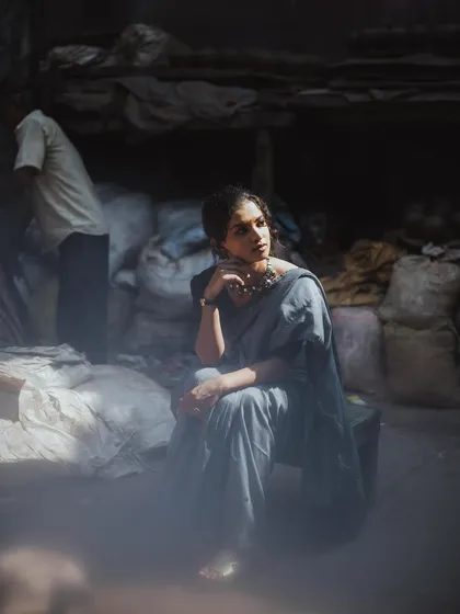 An atmospheric shot using a hazy, layered effect. The model is seated in a rustic warehouse-like setting, creating a portrait that feels both industrial and deeply personal.