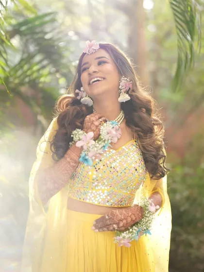 A sun-kissed photo of the bride, glowing with happiness. The soft light highlights the delicate details of her floral necklace and earrings.