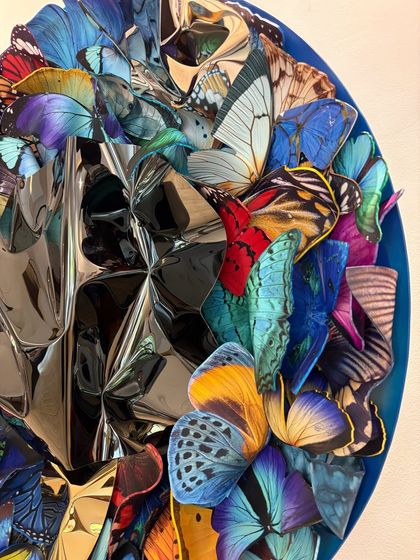 A detail of "Metamorphosis in Metal," showing the contrast between the colorful, delicate butterfly wings and the hard, reflective metal.