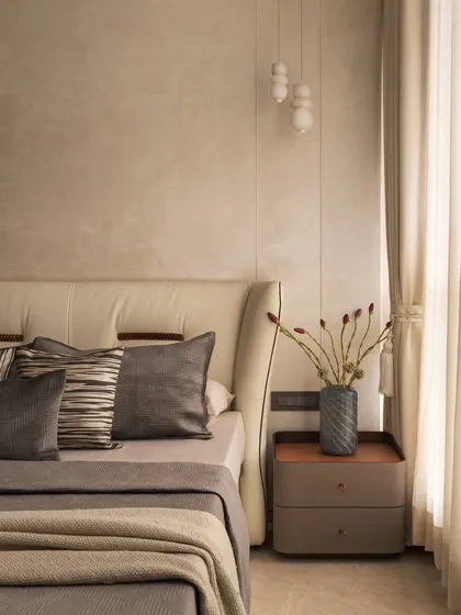 A close-up of the bedside styling. A sculptural vase with dried stems sits on a modern nightstand, perfectly complementing the textures of the wall and the layered pillows on the bed.