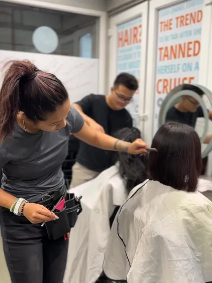 A student practices her cutting technique on a live model, with an instructor providing guidance. This personalized attention is a core part of our teaching method.