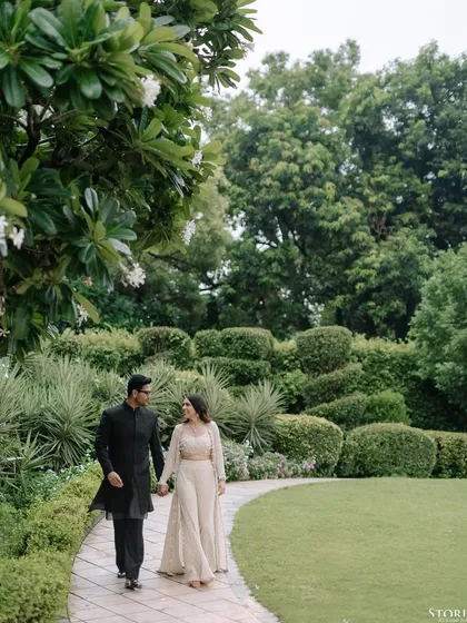 A wide shot of the couple walking on a path in a garden, capturing the beautiful landscape and their romantic stroll.