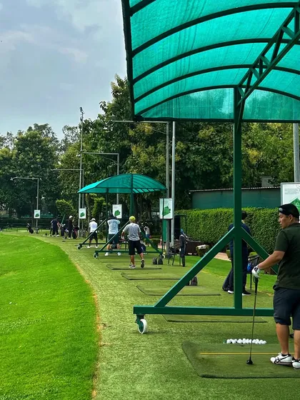 A golfer pauses to watch his shot, standing at his bay with a fresh bucket of balls ready to go.
