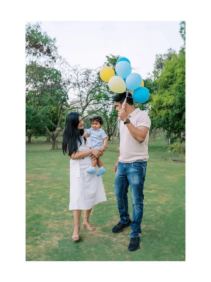 A family enjoying their outdoor birthday shoot with balloons. The wide framing captures the beautiful park setting.
