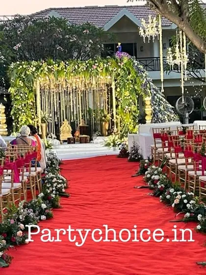 We use vibrant colors to make your wedding path memorable. Here, a bright red carpet aisle is lined with floral arrangements on the chairs, leading guests' eyes directly to the stunning peacock-themed mandap.