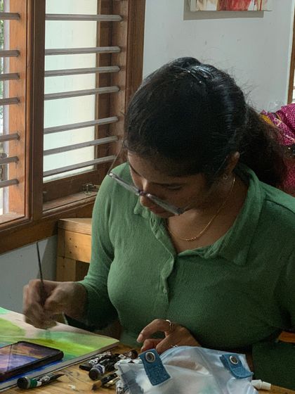 A student works on a landscape painting, carefully adding details to the foliage. The process requires patience and a steady hand, skills we help nurture.