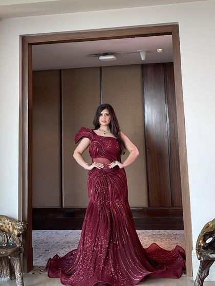 A full-length shot of the red sculpted gown. The dress features a sheer panel at the waist and a one-shoulder design, combining modern details with a classic mermaid shape.