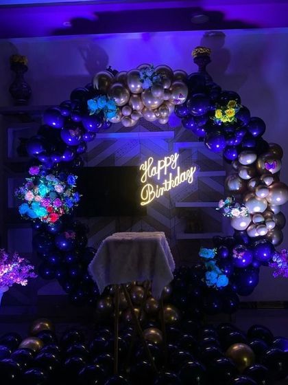 A dramatic birthday setup with a blue and gold balloon ring under purple lighting.