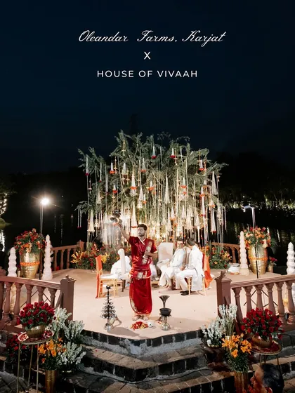 The priest performs rituals at the unique mandap built around a tree on a raised platform over water, glowing under the night sky at Oleander Farms.