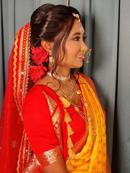 A side profile of Priyanka's Bengali bridal look, showing the messy bun adorned with red flowers and the intricate 'nath' (nose ring).