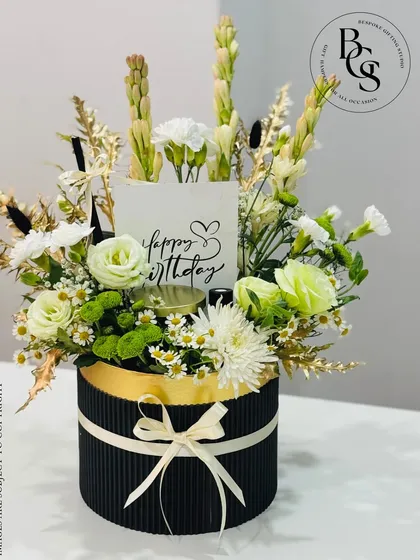 A beautiful birthday floral arrangement in a black corrugated hatbox. The white and green flowers are accented with a "Happy Birthday" card, offering a fresh and elegant birthday greeting.