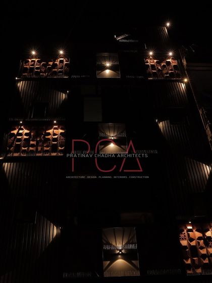 A night shot focusing on the illuminated terracotta jaalis and the PCA brand logo on the Chadha Properties office facade. This highlights the intricate details that come to life with lighting.