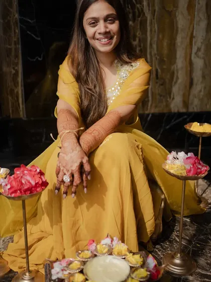 A happy bride surrounded by flowers, with her beautiful dark mehendi stain on full display.