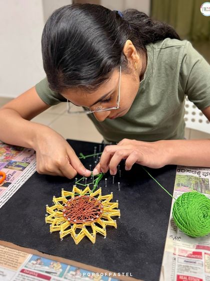 Deep in concentration, this participant meticulously weaves green and yellow string to form the petals of a beautiful sunflower.