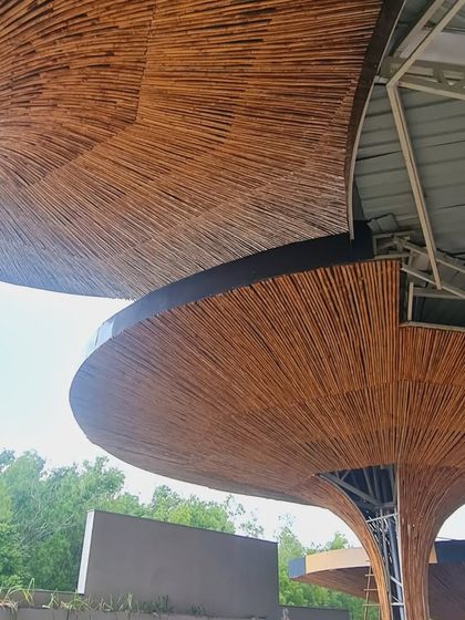 A view from below of the overlapping bamboo parasols during construction, showcasing the intricate craftsmanship and the scale of the structures.