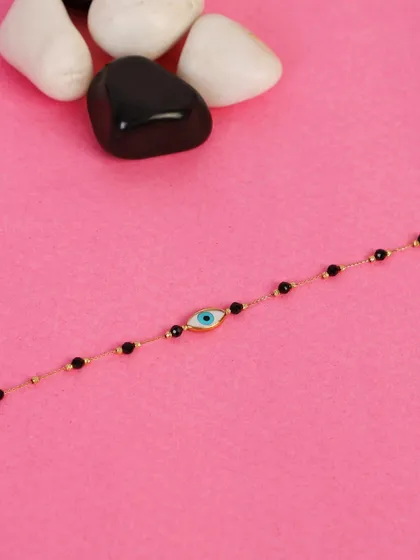 A women's evil eye bracelet styled on a pink background with smooth black and white stones. Using props helps to create a visually interesting and high-end look for jewelry.