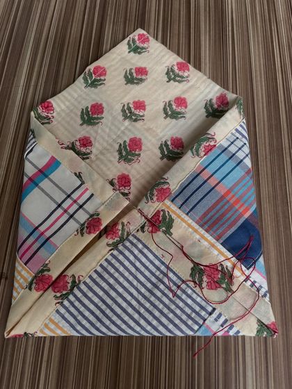 The patchwork pouch in progress, with a needle and thread still attached. This shows the hands-on process of combining different fabrics and adding decorative stitches.