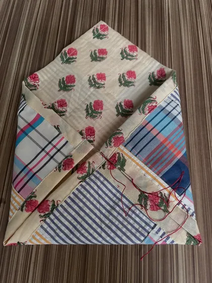 The patchwork pouch in progress, with a needle and thread still attached. This shows the hands-on process of combining different fabrics and adding decorative stitches.