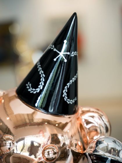 A close-up of the "Let’s Party Teddy" sculpture, focusing on the detailed party hat and the reflective rose gold chrome finish.